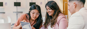 Three students sat at a table looking at a shared laptop screen