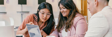 Three students sat at a table looking at a shared laptop screen