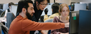  Two students looking at a computer with a lecturer