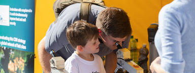 A child and an adult look through a microscope at Pop Up University 2021