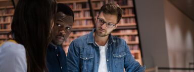 Three people in a library discuss an exhibition
