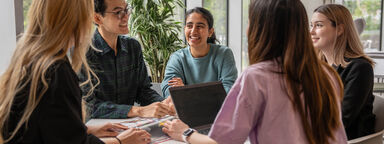 A group of postgraduate students sat around a table smiling and chatting