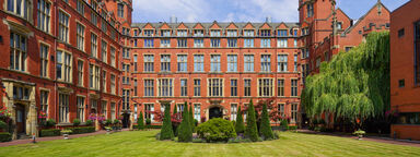 image shows the quadrangle of Firth Court. Firth Court is a traditional red brick university building and quad features a lawn, trees and central water feature.