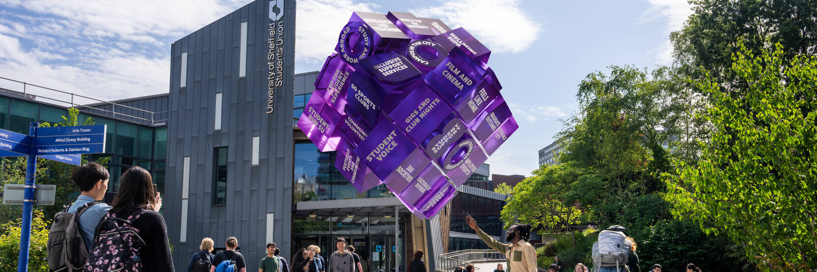 Students next to Sheffield Students' Union and looking at a purple cube