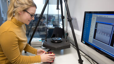 Postgraduate physics student in yellow jumper working with equipment at computer