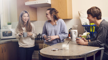 Three students sat in their kitchen laughing 