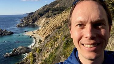 Dr Tom Darton on top of a cliff with water in the background. 