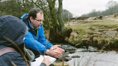 A technician instructs a student by a river