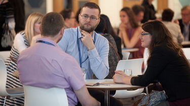 Participants at a conference. Three academics discussing ideas while sitting at a table.