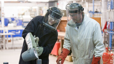 Student pouring metal under supervision by tutor