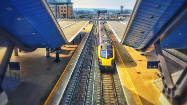 A train passes through a railway station. It is sunny. 