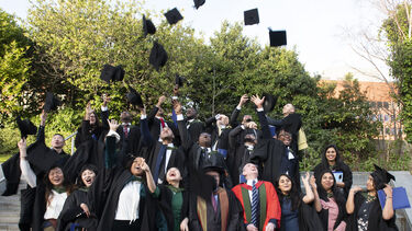 A group of graduates throw their hats. They are on a staircase.