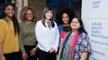Five female students outside of the School of Health and Related Research building, next to a sign stating the building's name.