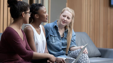 Three female PGT students in conversation about a project. They are gathered around a laptop. 