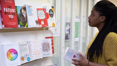 A student in a yellow jumper inspects the bookshelf in the School of Health and Related Research library. 