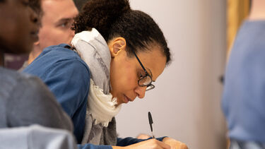 A student taking notes with a pen and paper in a School of Health and Related Research lecture.