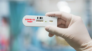 Gloved hand holding a positive Covid-19 blood test