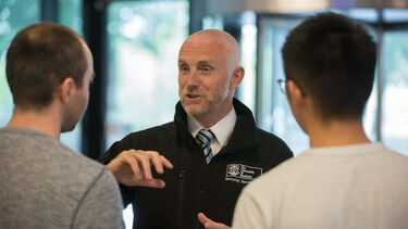 A member of security talking to two students