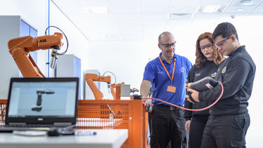 Two students are looking at a tablet, while a AMRC worker helps them - image