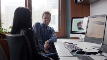 Phd student and supervisor reviewing research on a computer.
