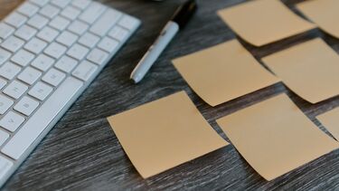 A keyboard, pen, and number of blank orange sticky notes on a desk