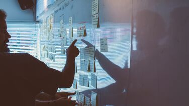 Person pointing to post-it notes on a white board