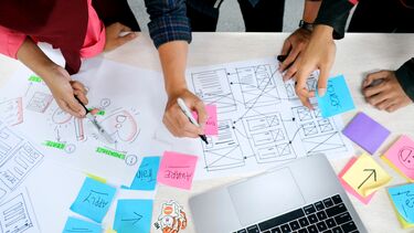 Three people working on a project with papers and a laptop on a desk.