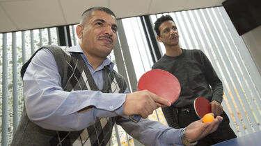 Students playing doubles table tennis, about to serve