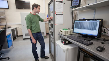 A man stood in a lab looking at a screen on the wall and flicking a switch underneath it.