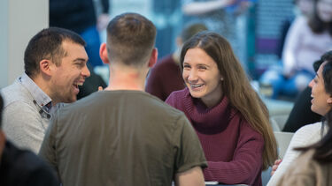 Four students laughing and sitting around a table in the courtyard café