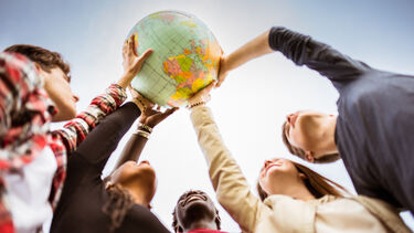 Students reaching up and holding a globe