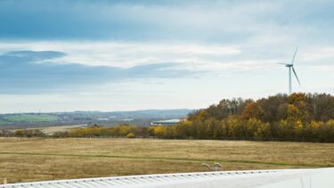 A scenic view looking across fields and trees with a wind turbine in the background