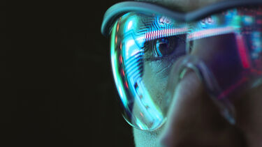 A close up of a woman's face wearing glasses with a circuit board reflecting in them