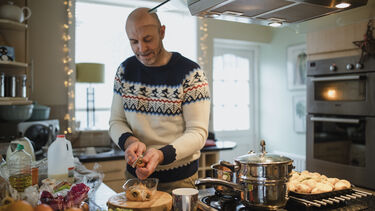 One mature man is preparing a christmas dinner in the kitchen of his home. He is peeling carrots and parsnips.