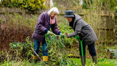 Two older women gardening. They are leaning in and looking at a plant.