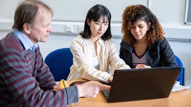 Teacher Pointing at Laptop being used by Two Students