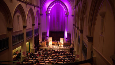 Large space with audience and purple back lit stage 