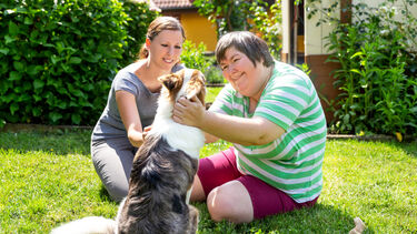 A picture of two people sat on the grass stroking a dog