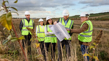five people in hard hats and hi-vis vests looking at building plans 