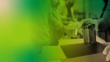 A volunteer places canned food into a cardboard box.