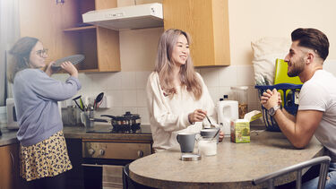 photo of students in kitchen, drinking tea and putting plates into a cupboard