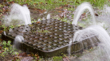 A man hole cover being pushed up under the force of water pressure during flooding 