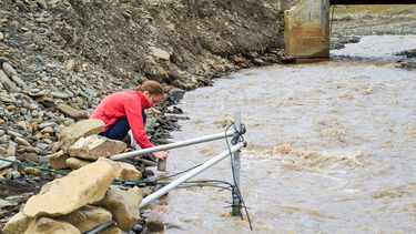 Person crouching on rocky bank to take river sample