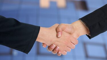 Two women shaking hands. They have suit jackets on.