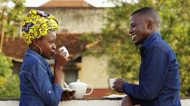 A photograph of a male and female Ugandan talking and sharing a pot of tea.