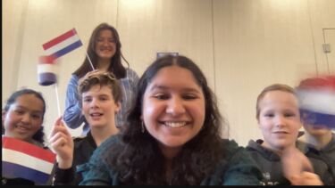 teacher surrounded by kids waving little Dutch flags. Everybody is smiling