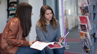 A photo of two students sat in the Employability Hub. They are reading through brochures and flyers.
