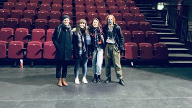 4 young people in a a theatre with red rows of chairs