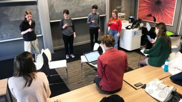 6 students and tutor in a play set up. They are all looking at their phone for the text