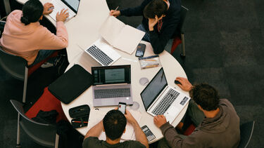 A view looking down on a group of students sat around a table working on their laptops
